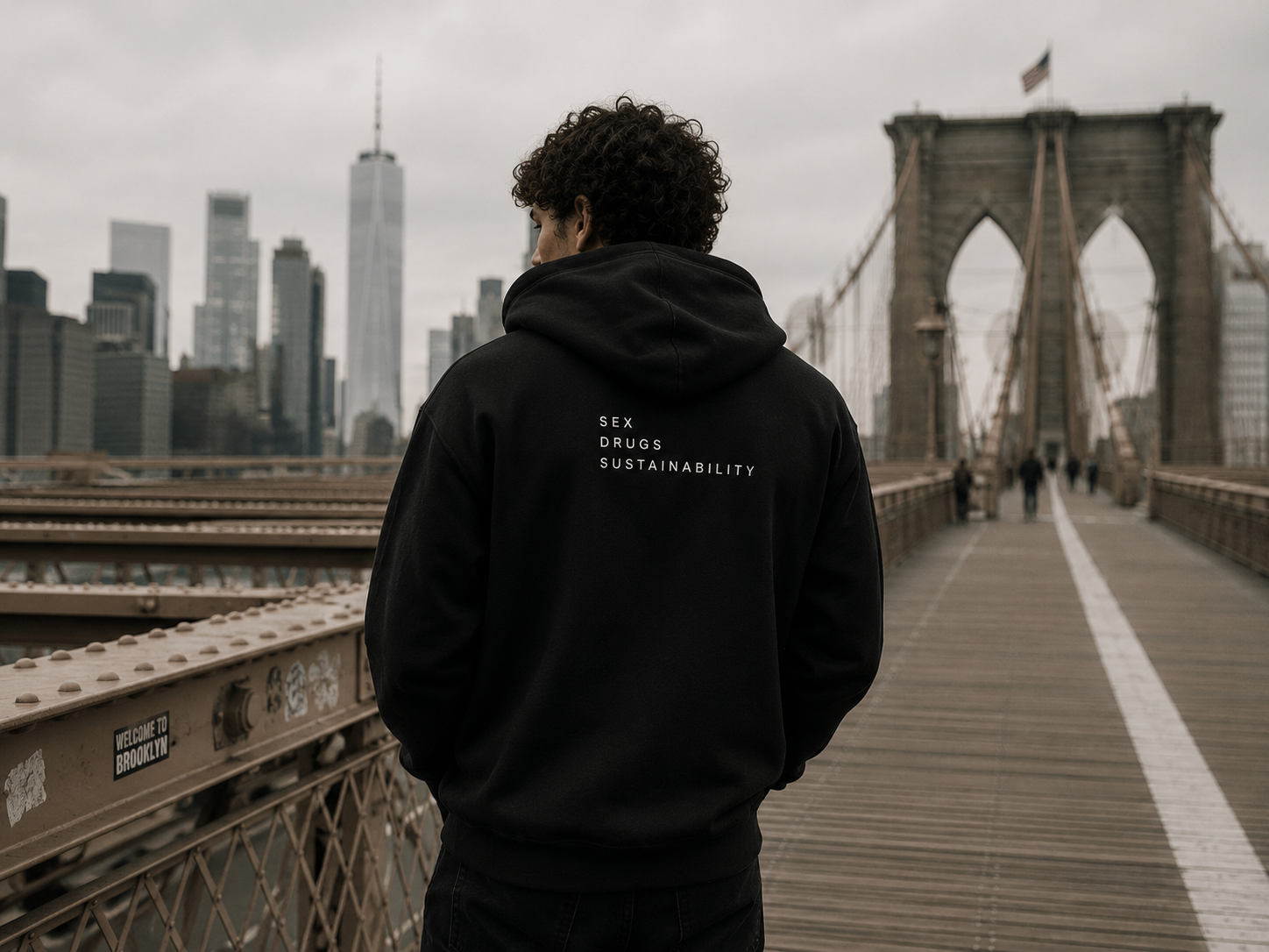 Model wearing black SDS hoodie on Brooklyn Bridge with New York skyline in the background